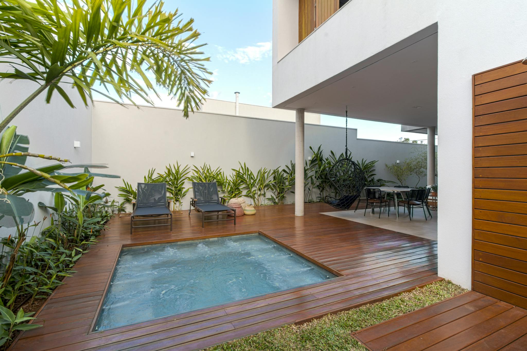 A serene modern patio featuring a luxurious jacuzzi, chic furniture, and lush greenery.